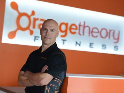 Dave Long, CEO de Orangetheory Fitness, posando con el logo de la empresa detrás